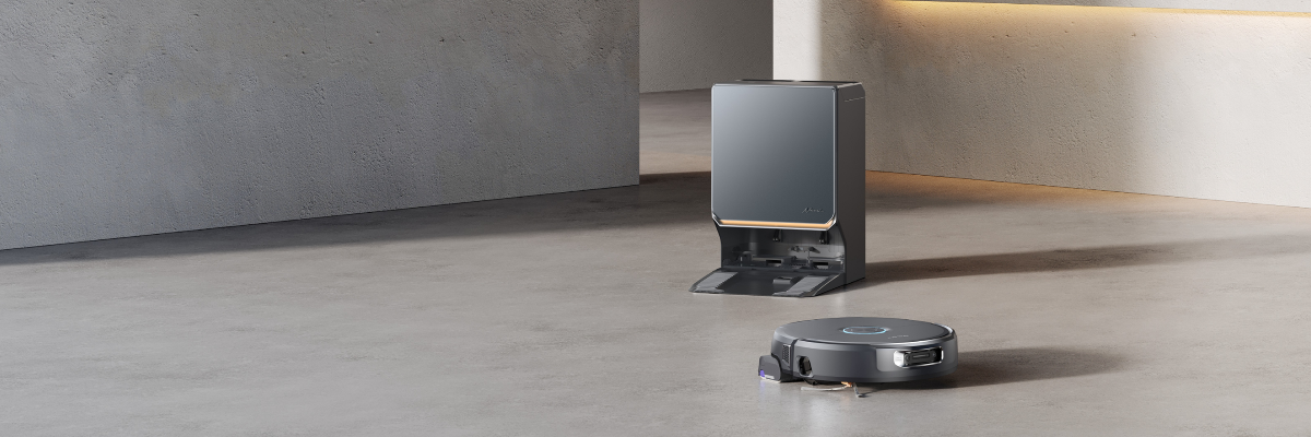 A robotic vacuum cleaner in a modern minimalist room with concrete floors and walls, positioned in front of its dark gray charging dock.